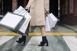 Bottom half of female consumer carrying shopping bags across a crosswalk