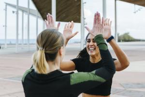 Color photo of one blonde and one brunette lady high-fiving one another