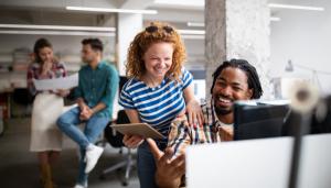 Stock color photo of a red-haired woman laughing with her male colleague in front of a monitor at an office