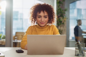 Photo of woman of color facing the camera and typing on a laptop