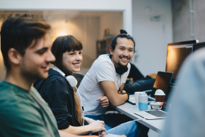 Color photo of 4 people seated around a desktop monitor smiling