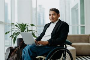 Color photo of Hispanic man in a wheelchair and holding a laptop