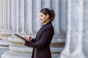 Color photo of woman standing with digital tablet in front of massive columns