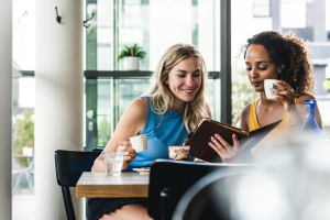 Two women drinking coffee and reading on a shared tablet