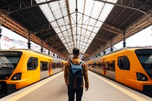 Color photo of man with backpack at a train station facing two trains
