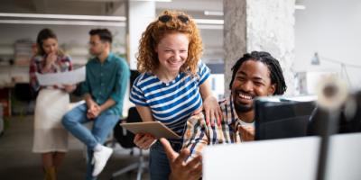 Stock color photo of a red-haired woman laughing with her male colleague in front of a monitor at an office