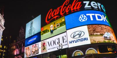 Color photo of multiple neon signs featuring brand logos affixed to a building