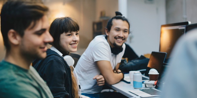 Color photo of 4 people seated around a desktop monitor smiling