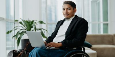 Color photo of Hispanic man in a wheelchair and holding a laptop