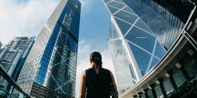 Color photo of the back of a woman looking up at skyscrapers