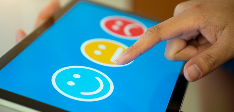 Person touching a digital screen with three smiley face icons