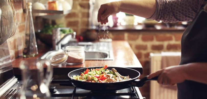 Frying pan over stove with hand spicing food