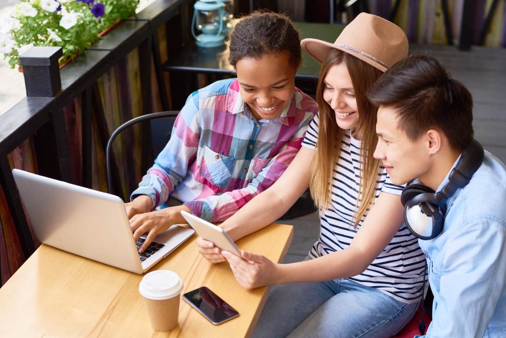 Three friends in cafe using digital devices