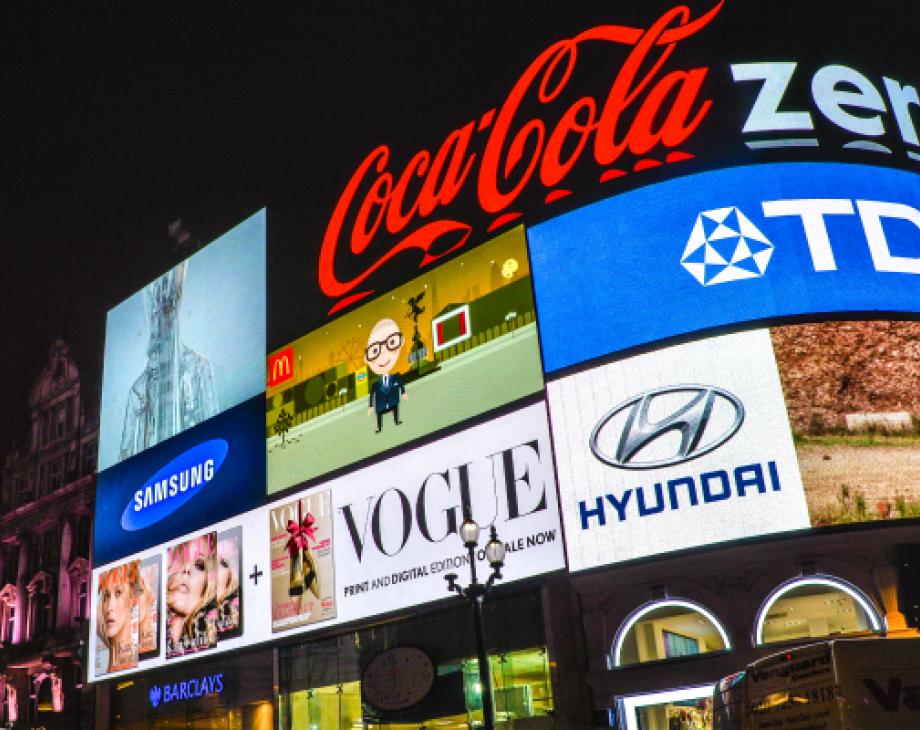 Color photo of multiple neon signs featuring brand logos affixed to a building