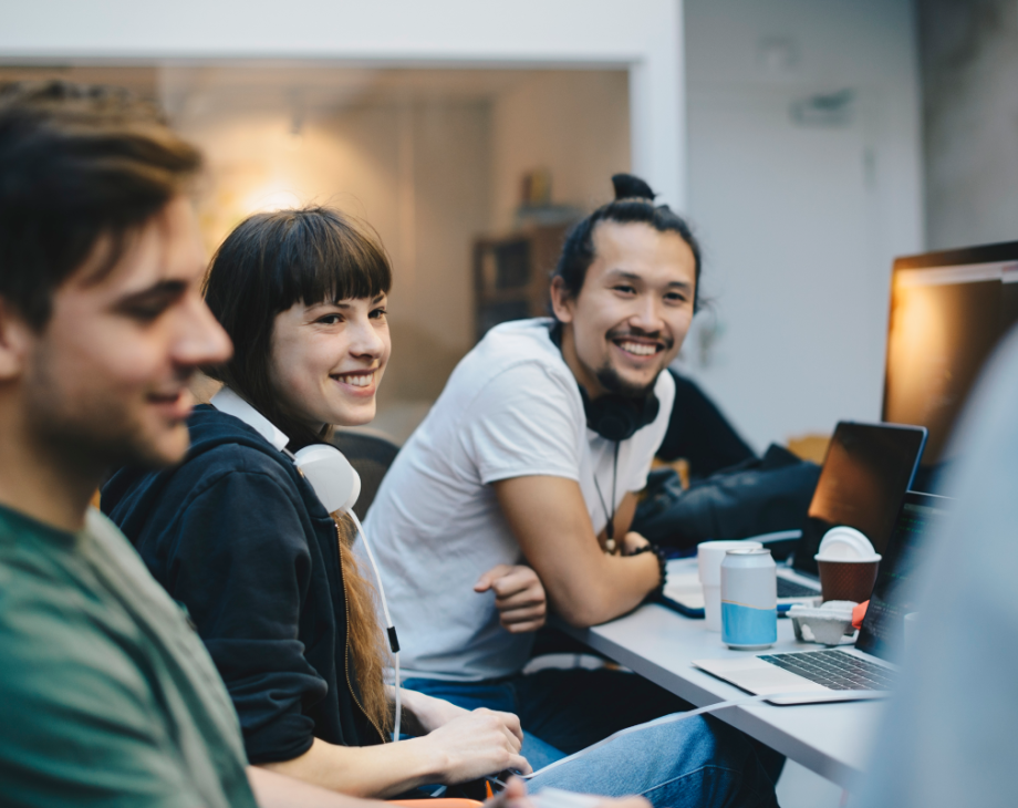 Color photo of 4 people seated around a desktop monitor smiling