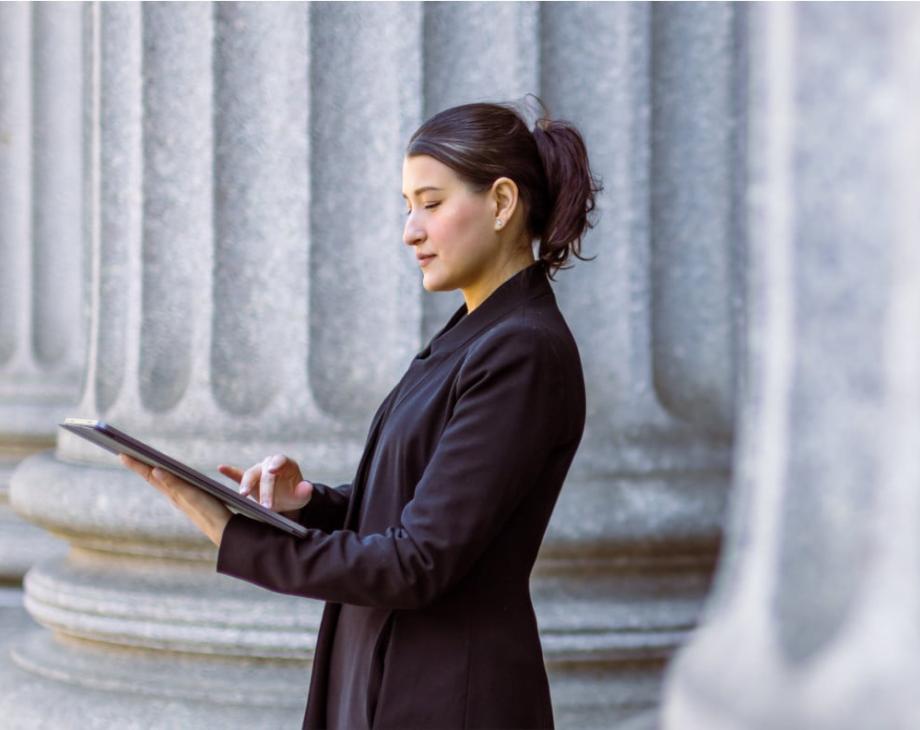 Color photo of woman standing with digital tablet in front of massive columns