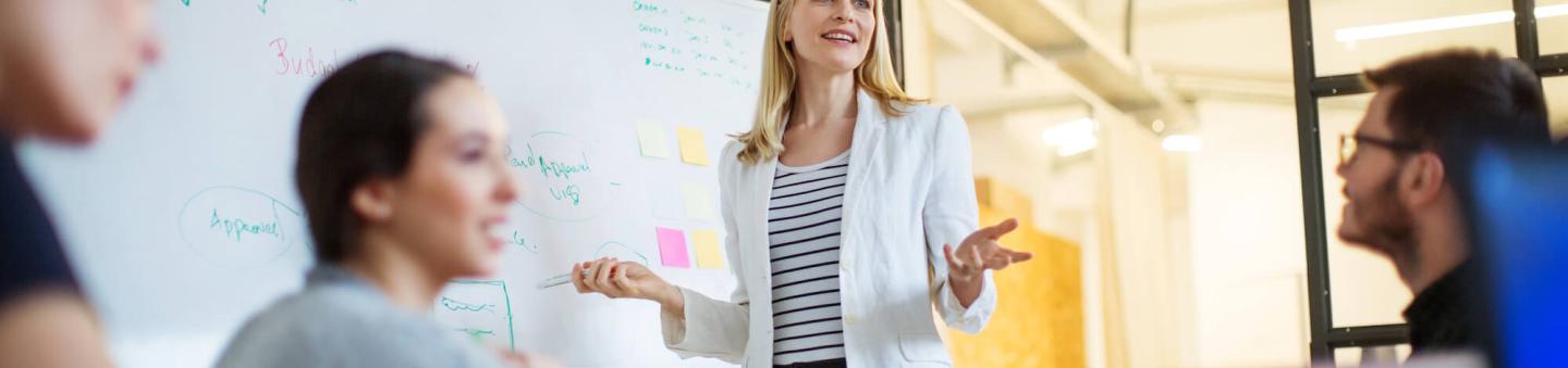 Female executive standing at whiteboard in front of coworkers