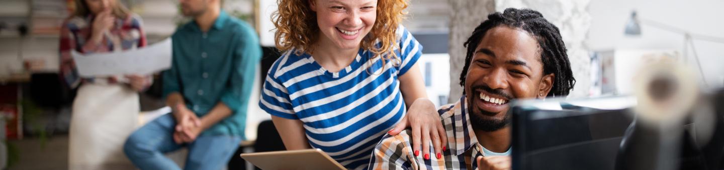 Two people laughing as they collaborate over a computer